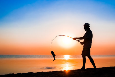 Happy guy fisherman catching fish by the sea on nature silhouette travelの写真素材