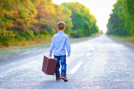 Happy child with a suitcase on the road in the park travelの写真素材