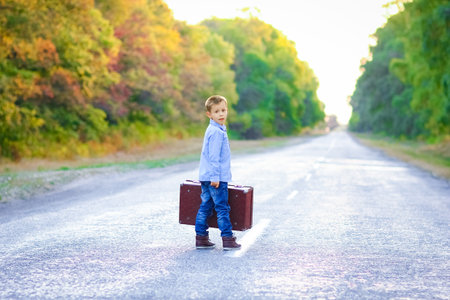 Happy child with a suitcase on the road in the park travelの写真素材