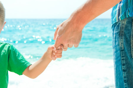 Hands of a happy parent and child on the seashore on a journey trip in natureの写真素材