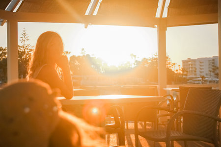 happy girl at a table by the sea at sunsetの写真素材