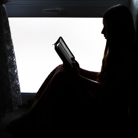 silhouette of a nice girl with a book near window