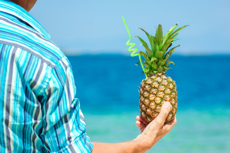 Pineapple in the hands of a man by the sea in nature on a journey backgroundの写真素材