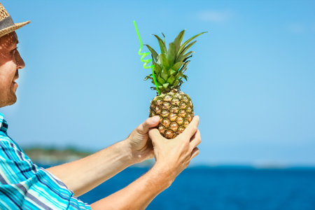 Pineapple in the hands of a man by the sea in nature on a journey backgroundの写真素材