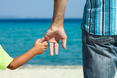 Hands of a happy parent and child on the seashore on a journey trip in natureの写真素材