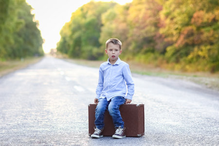 Happy child with a suitcase on the road in the park travelの写真素材