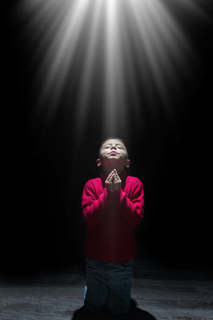 Child praying spiritually to God on a black backgroundの写真素材