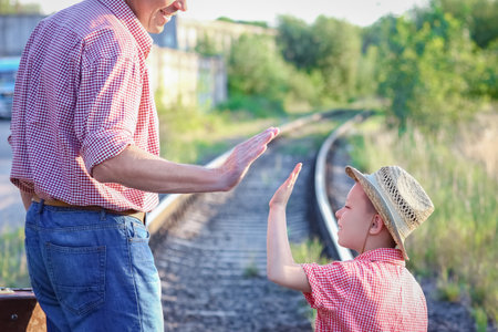 hands of parent and son in cowboy hat near the railroad with suitcaseの写真素材