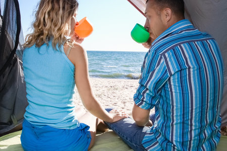 Happy couple looking out of tent at sea on travelの写真素材