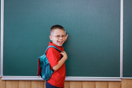 Happy child child standing at the blackboard with a school backpack wearing glassesの写真素材