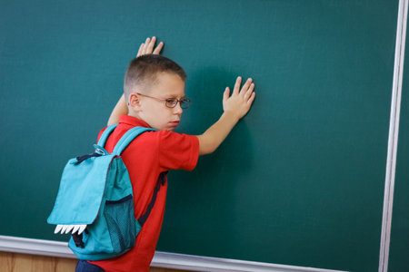 Happy child child standing at the blackboard with a school backpack wearing glassesの写真素材