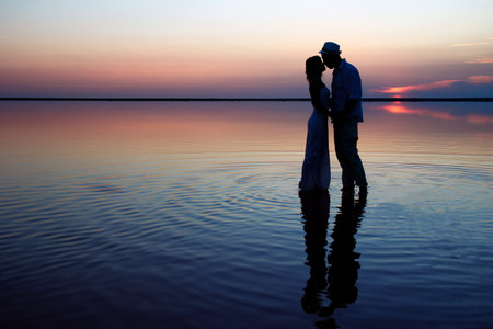 happy couple at sea with water reflection silhouette backgroundの写真素材