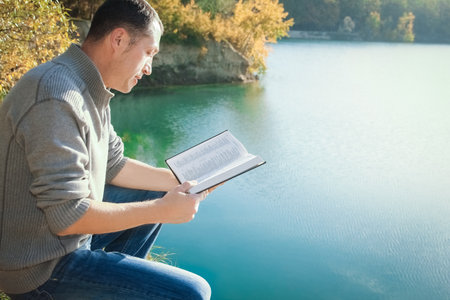 Happy guy reading a book in the park on nature travel educationの写真素材
