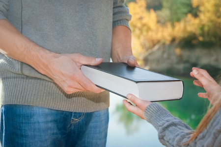 From hand to hand a parent passes a book to a child in a park outdoors travelの写真素材