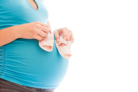 pregnant girl on a white background with children shoesの写真素材