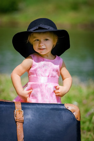 Happy baby girl with a suitcase outdoors at the parkの写真素材
