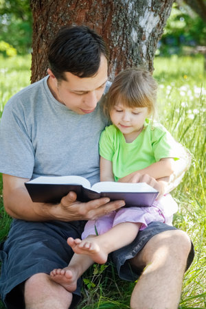 happy father with a child reading a book on the nature of the Bibleの写真素材