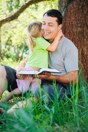 happy father with a child reading a book on the nature of the Bibleの写真素材