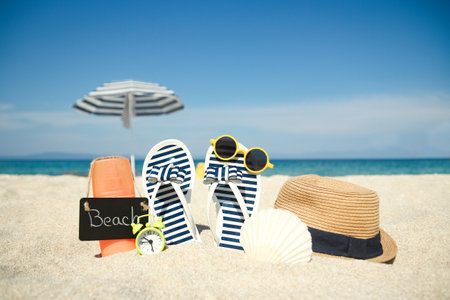 Beach summer holiday banner background. Flip-flops and hat with a board and ball on the sand near the ocean. Summer accessories on the seashore. Tropical vacation and relax travel concept. Top view and copy space.の写真素材