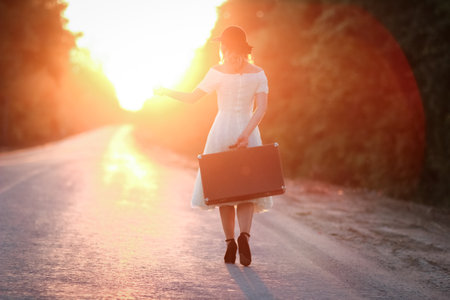 vintage girl with hat with a suitcase hitchhikingの写真素材