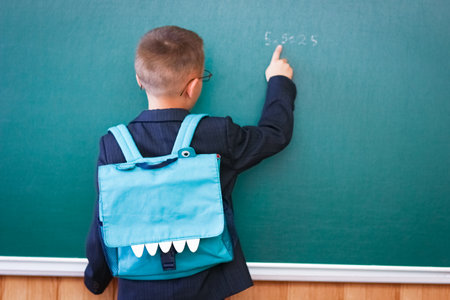 Happy child child standing at the blackboard with a school backpack wearing glassesの写真素材