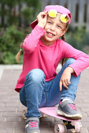 happy little girl in sunglasses on skateboardの写真素材