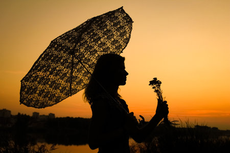 Happy girl with an umbrella silhouette on nature in the park sunsetの写真素材