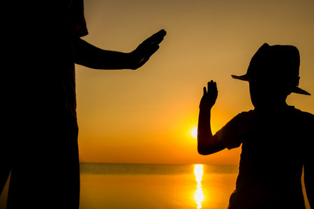 Hands of happy father and child by the sea on nature silhouette travelの写真素材