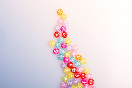 Multi color alphabet letter beads placed randomly on white background