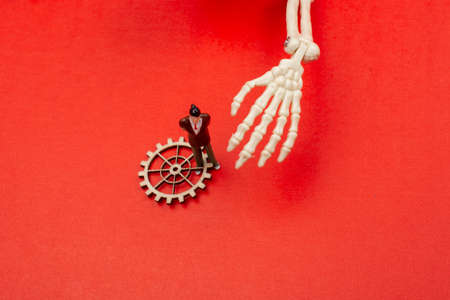Skeleton hand pressing on man figurine on red .  Death conceptの写真素材