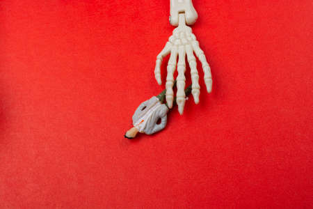 Skeleton hand pressing on man figurine on red .  Death conceptの写真素材