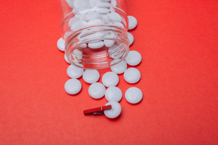 White medical pills spilling out of pills bottle, red background.  Medications and Phramacy.の写真素材