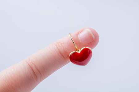 Red color heart shape earring in hand on whiteの写真素材