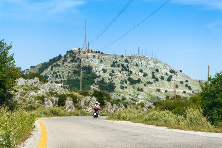 Road leading to the rocky highest peak Pantokrator, young people ride a motorbike.の写真素材