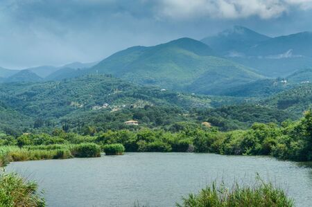 A riverbed at the foot of green mountains, a storm is coming to the mountain peaks.