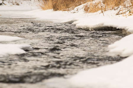 Frozen banks of the riverbed, water flows in the middle.の写真素材