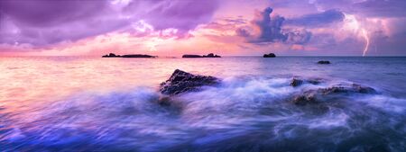 Colorful calm sea during sunset. A storm is approaching over the horizon. Colorful dark clouds in the air, electric discharges herald the coming storm.の写真素材