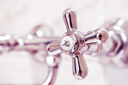 Bathroom faucet with hot water tap, made of stainless steel. The tap is attached to the tiled wall.の写真素材