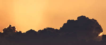 Dark storm clouds lit by the setting sun, the sun's rays illuminate the sky in yellow.