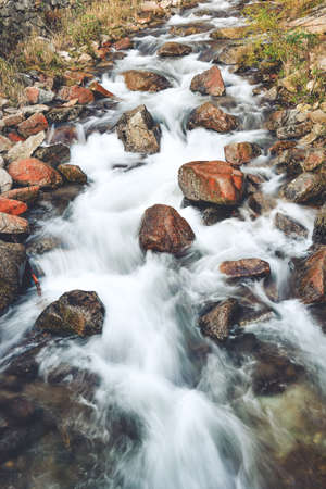 Rapid mountain river in the forest. After the rain, the river has risen and flows downhill in a strong stream. River bed with foaming water and numerous stones.の写真素材