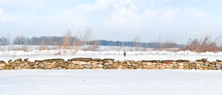 A stone fence covered with white snow on a sunny day.の写真素材