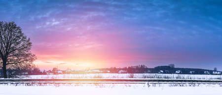 Colorful winter sunset on a cloudy evening over the village of Siedlec. View from the snow-covered road next to the railway tracks.の写真素材