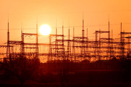 Power lines, high masts for electricity transmission, view at sunset with the sun.