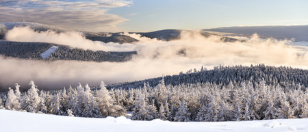 Through the valleys, the fog climbs the snow-capped mountain range of the Snieznik Massif just...