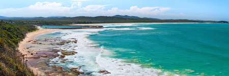 Australian coast, view from a cliff of the blue ocean and a rocky shore with a sandy beach. Small bay with volcanic rock, sunny day.の写真素材
