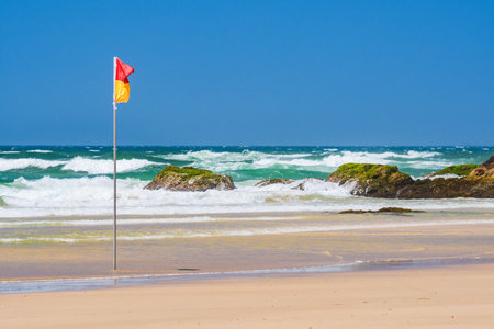 Red and yellow flag of lifeguards on the beach, rough ocean with high waves, seaside landscape on a sunny summer day.の写真素材
