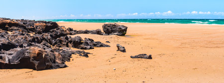 Australian coast with dark volcanic rocks on a wide sandy beach, sunny summer day.