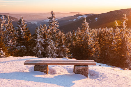 Sudetes, a bench with a view of the mountain landscape at sunset, a view from the hiking trail in winter.の写真素材