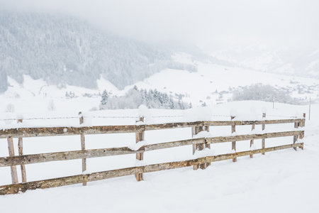 Snow-covered wooden fence on a mountain pasture. Winter landscape on a mountain hiking trail on a cloudy and foggy day.の写真素材