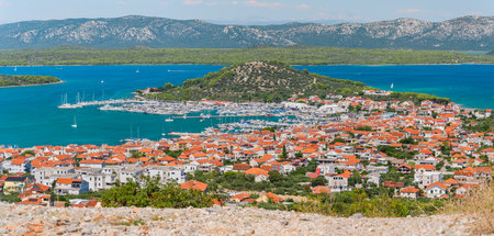 The coastal town of Murter in Croatia is situated on the seashore with a mountain landscape, seen...